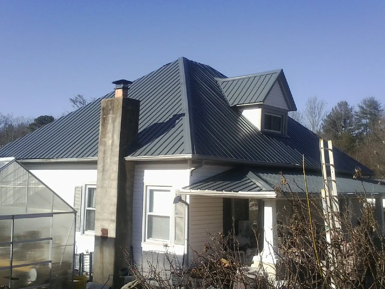 Dark blue standing seam metal roof on a white farmhouse with dormer — Slate & Tile Roof Repair by Roofing Brothers in Fort Ogden