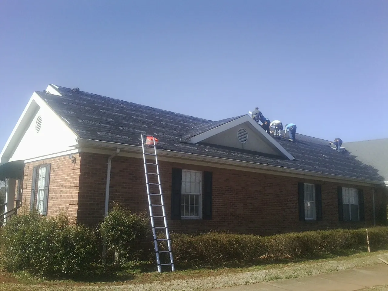 Crew tearing shingles off a brick ranch roof with a ladder set — Metal Roof Repair work by our crew in Fort Ogden