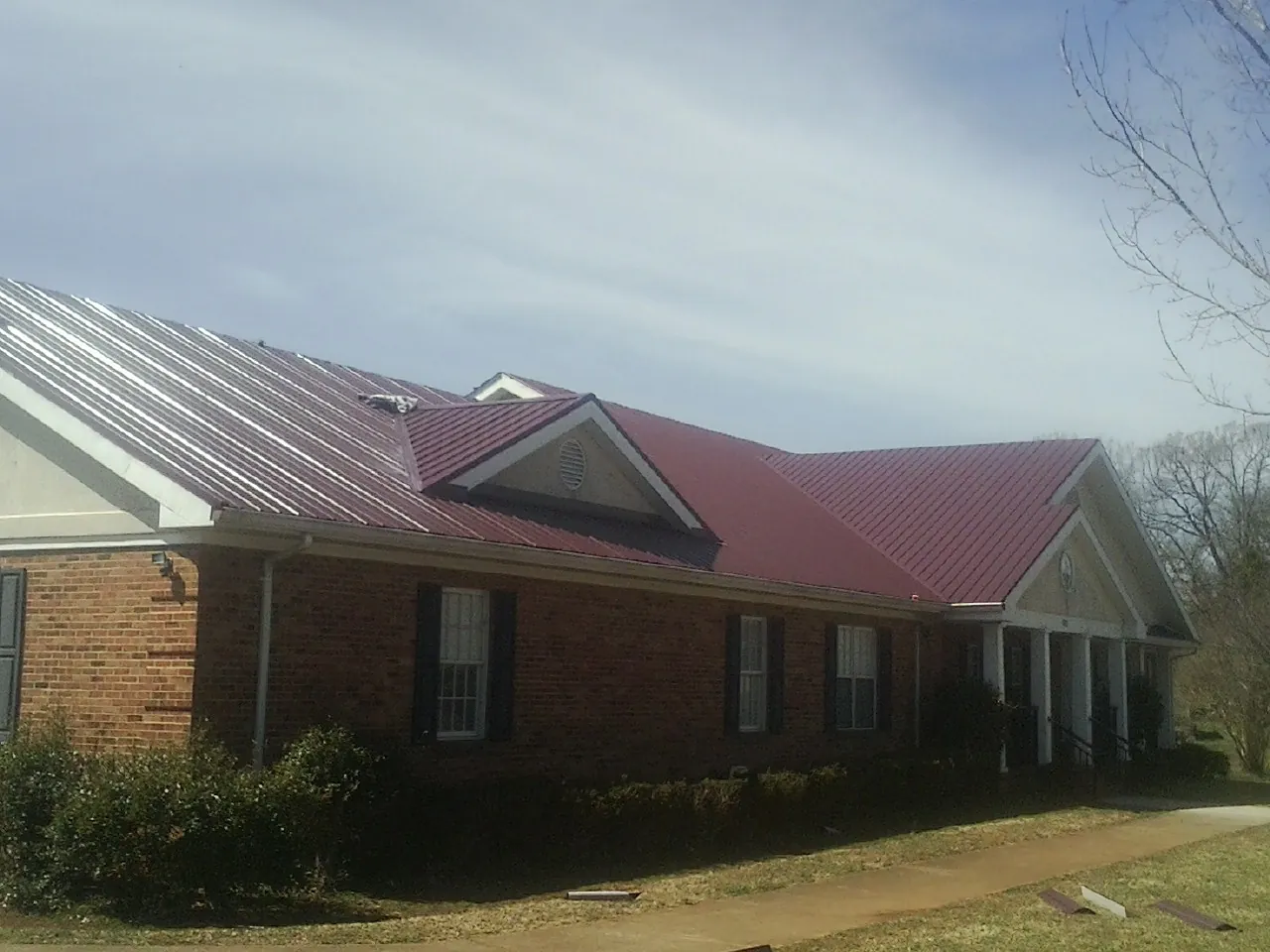 Red metal roof with gabled entries on a long brick building, from a Hail Damage Roof Repair job in Fort Ogden