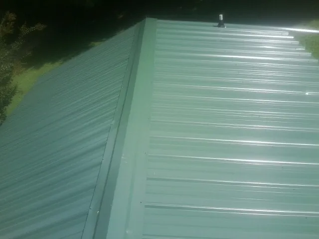 New green metal panels meeting at the ridge of a roof — Flat Roof Repair work by our crew in Fort Ogden