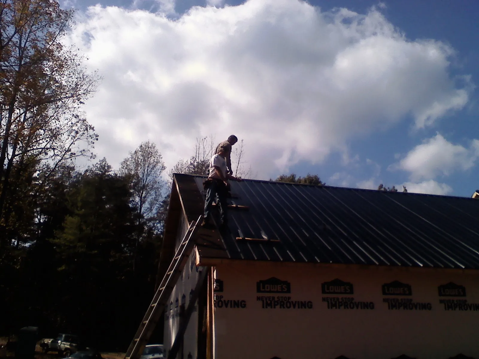 Roofer fastening dark metal panels high against a cloudy sky, from a Roof Inspection job in Fort Ogden