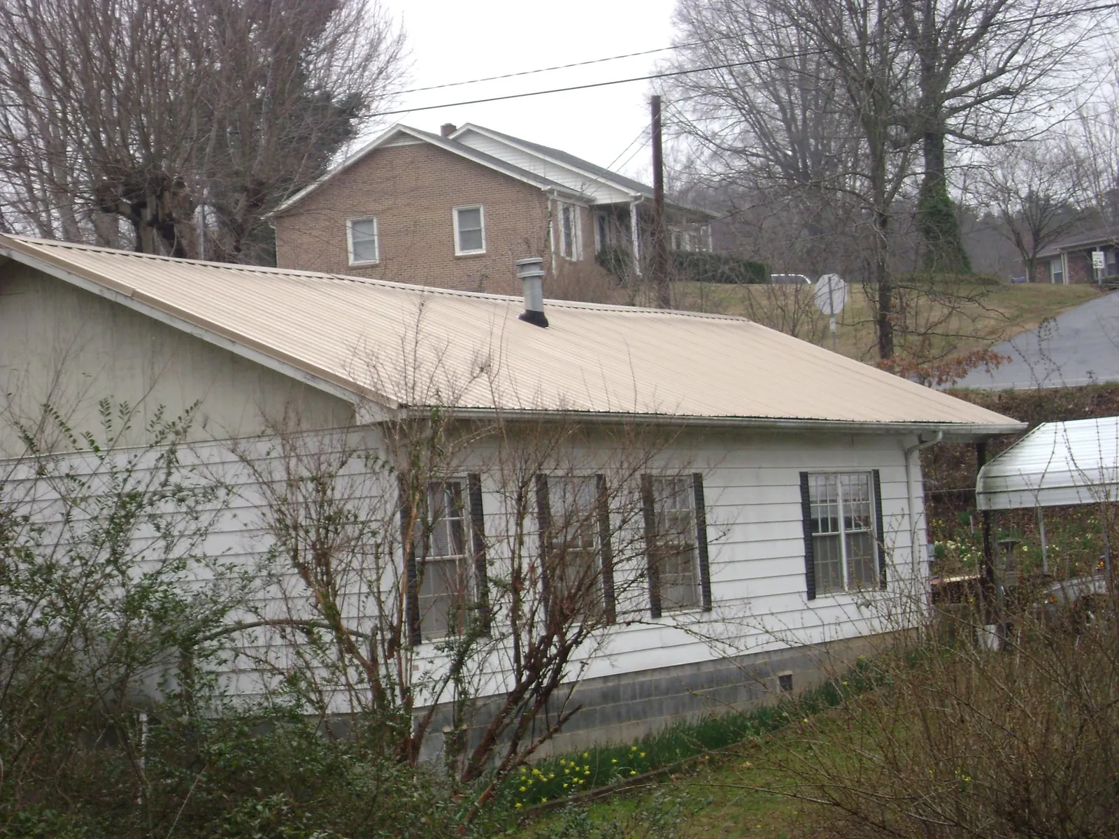 Tan metal roof on a white sided house set into a hillside — Commercial Roofing by Roofing Brothers in Fort Ogden