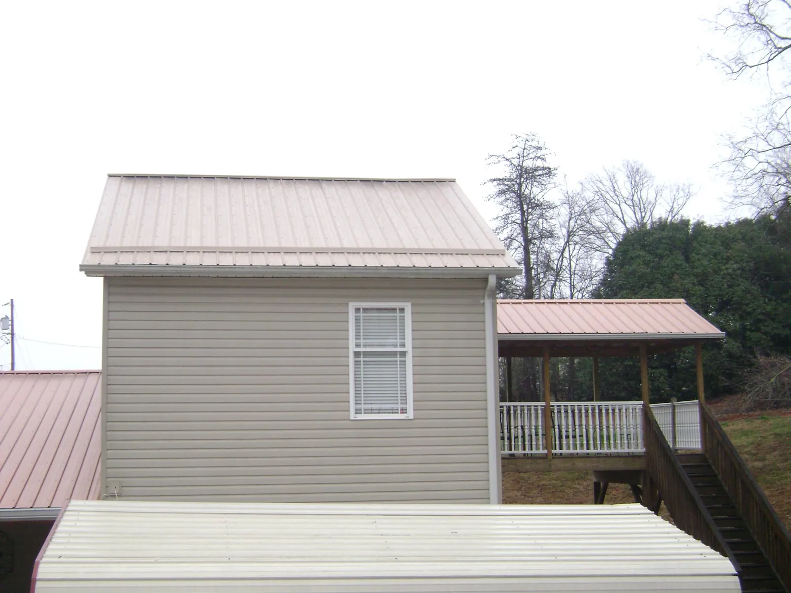 Tan metal roofs on a two story addition and attached porch, from a Roof Replacement job in Fort Ogden